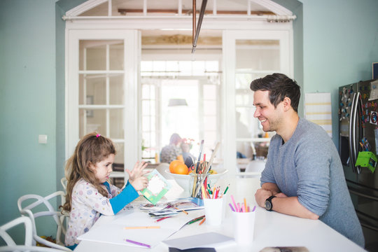 Smiling father looking at girl holding picture book in kitchen