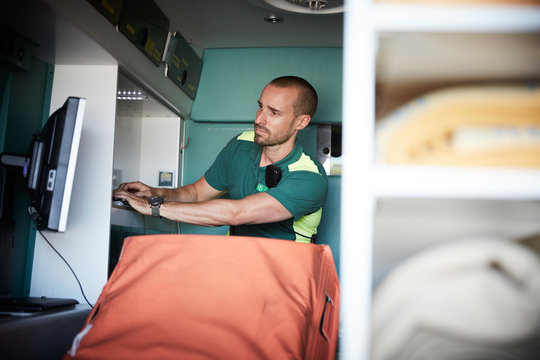 Male paramedic typing while looking at monitoring screen in ambulance