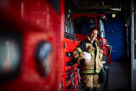Portrait of smiling firefighter with helmet standing by fire engine at fire station