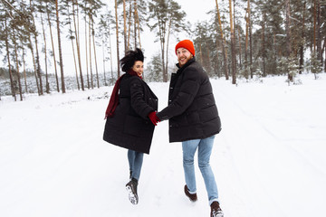 Loving young couple in winter stylish clothes walks in a beautiful winter forest holding hands