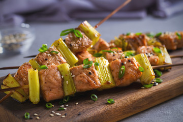 Skewered salmon teriyaki with leeks, sprinkled with sesame seeds on serving board. Horizontal image