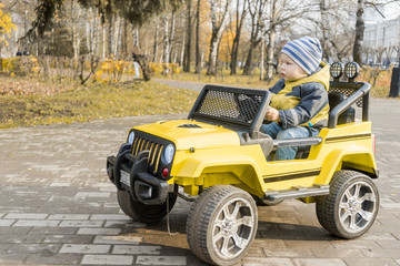 Fototapeta na wymiar toddler on yellow children drive car with an electric motor in autumn Park