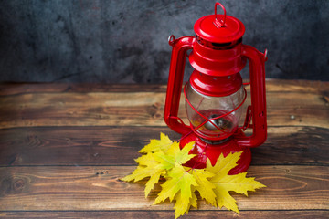 Red kerosene lamp with autumn leaves on a dark background.