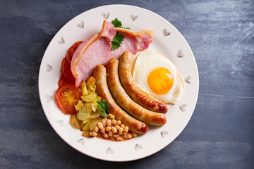 Full English or Irish breakfast with sausages, bacon, egg, tomatoes, fries and beans. Nutritious and healthy morning meal. View from above, top studio shot