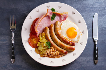 Full English or Irish breakfast with sausages, bacon, egg, tomatoes, fries and beans. Nutritious and healthy morning meal. View from above, top studio shot