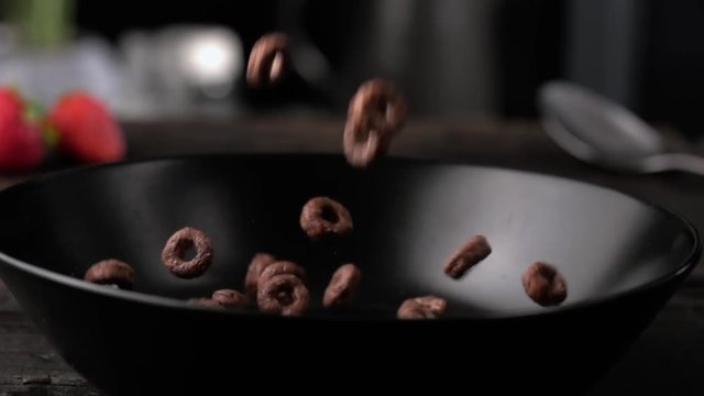 Chocolate breakfast cereal in black plate, morning food in slow motion side view