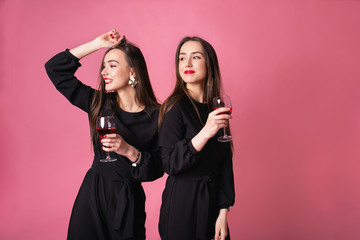 Two attractive women in night dress drinking wine isolated on a plastic pink background