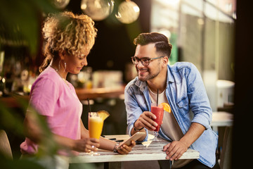 Happy couple drinking cocktails and using cell phone in a bar.