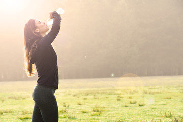 Fitness girl drinking water on a foggy and shining morning. Jogging
