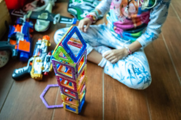 Little girl playing to build a tower with magnetic pieces of plastic colors.