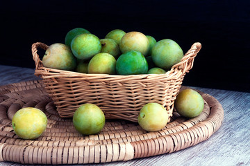 GREEN PLUMS IN WICKER BASKET ON DARK FUND. HEALTHY FRUIT