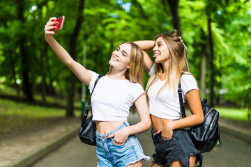 Friends making selfie. Two beautiful young women making selfie in park