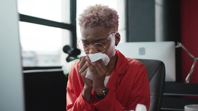 Portrait of sick poor afro-american business woman sneezing allergy coughing into napkins suffering virus flu in office workspace.