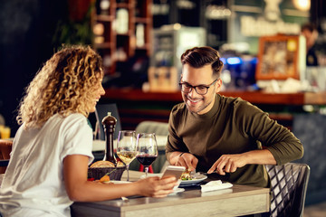 Happy couple using mobile phone during lunch time in a restaurant.