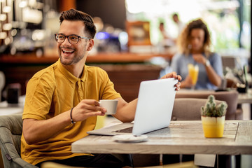Cheerful man having fun while using laptop in a cafe.