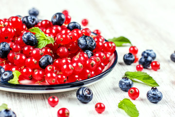 Fresh blueberries and red currants with mint leaves in a wooden bowl on burlap. Diet food, vegan berries