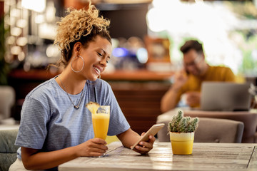 Young happy woman relaxing in a bar and texting on mobile phone.