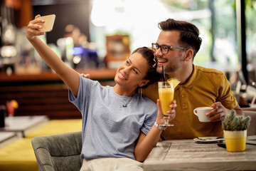 Happy couple using smart phone and taking selfie in a cafe.