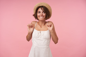 Studio photo of happy brunette woman with short haircut looking aside positively and biting her...