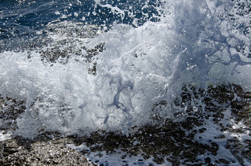 A wave breaks on a rock on a sunny day.