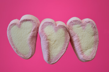 three white hearts with pink margin of marshmallow set against a pink background with free space