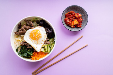 Korean bi bim bap and kimchi with chopsticks on pink background. Top view.