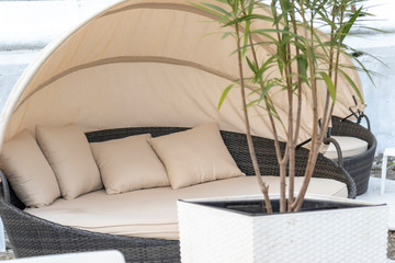 Relaxing brown rattan bed, sofa with beige pillows, sheet and roof on the beach, seashore