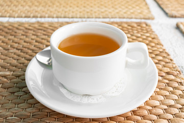 A white cup of green tea on a table covered with woven straw napkin in restaurant