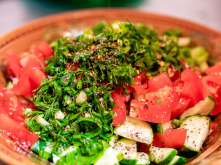 Salad of fresh tomatoes and cucumbers with herbs and spices in a deep round brown ceramic plate. Healthy vegetable diet food. Source of vitamins and fiber.
