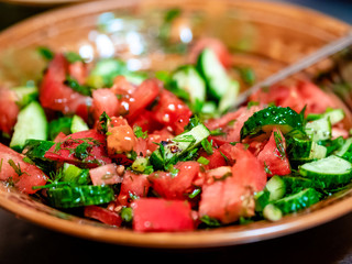 Salad of fresh tomatoes and cucumbers with herbs and spices in a deep round brown ceramic plate. Healthy vegetable diet food. Source of vitamins and fiber.