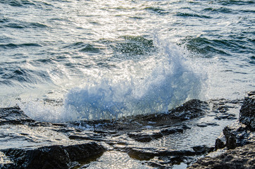 A wave breaks on a rock on a sunny day.