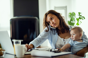 Young working mother talking on the phone and using computer at home.