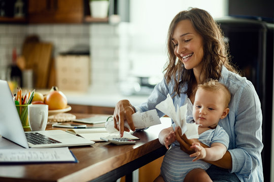 Happy mother with baby son calculating bills at home.