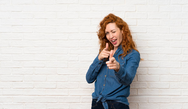 Redhead woman over white brick wall pointing to the front and smiling - Powered by Adobe