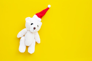 Toy bear wearing a santa hat on yellow background. Christmas holidays concept