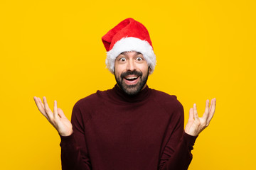 Man with christmas hat over isolated yellow background with shocked facial expression