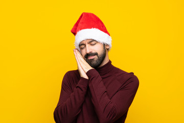 Man with christmas hat over isolated yellow background making sleep gesture in dorable expression