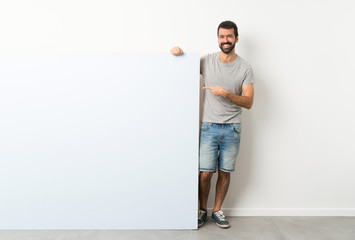 Young handsome man with beard holding a big blue empty placard pointing finger to the side