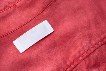 White blank clothing tag label on red linen shirt fabric texture background