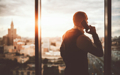 Silhouette of a prosperous man entrepreneur standing near the panoramic window of a luxurious...