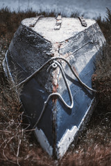 A vertical shot with a shallow depth of field of an old beautiful bluish wooden fishing boat put upside down with a rope on it and surrounded by a dry grass of a riverside, Alcochete, Portugal