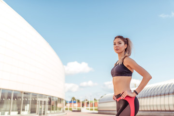 Young and athletic woman standing in city on summer, background building, sportswear. Athletics training, day morning. Active fitness lifestyle, free space for text motivation.