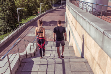 Young athletic couple man woman, walk on stairs, in summer jogging city, view from back, sportswear. Athletics training, day morning. Active fitness lifestyle, free space text motivation.