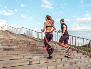 Young athletic couple man woman, jogging stairs morning, summer city, sportswear. Workout athletics, afternoon running. Active fitness lifestyle. Strength motivation. Free space text, view from rear.