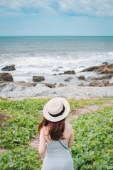 Fototapeta na wymiar Girl in straw hat standing backwards and looking at the sea
