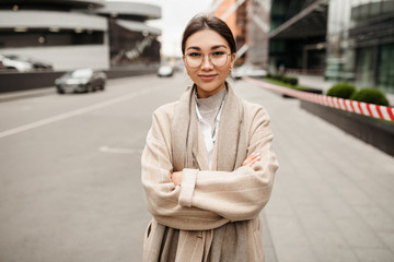 A beautiful girl of Asian appearance stands with folded hands in the middle of the business district