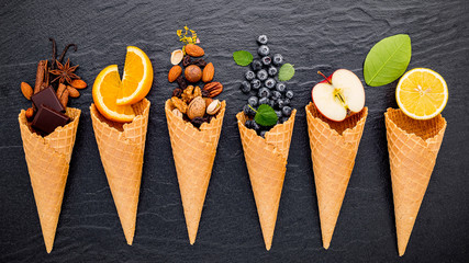 Various of ingredient for ice cream flavor in cones blueberry ,lime ,pistachio ,almond ,orange ,chocolate ,vanilla and coffee set up on dark stone background . Summer and Sweet menu concept.