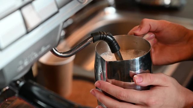 A woman is preparing coffee in a coffee machine. Close plan of the hands. Barista heats milk for a cappuccino in a cafe. The cuisine in the restaurant.