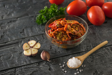Glass bowl with roasted tomatoes on the background of fresh on the wooden table. Vegetarian food.