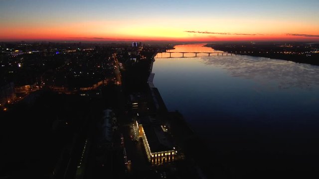 Aerial dark view of the night city on a wide river with a bridge at sunset.The sunset is reflected in the water.4k.Copy space